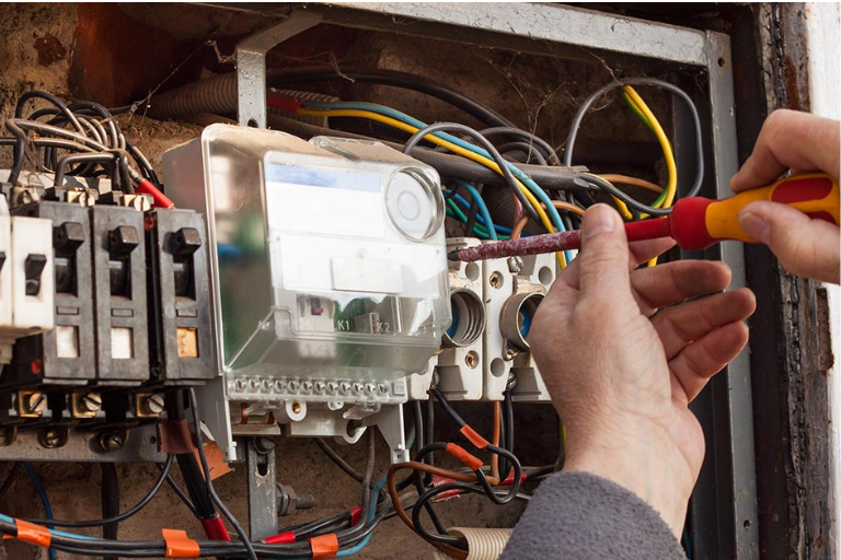 Person using a screwdriver to work on an electrical meter inside a panel.